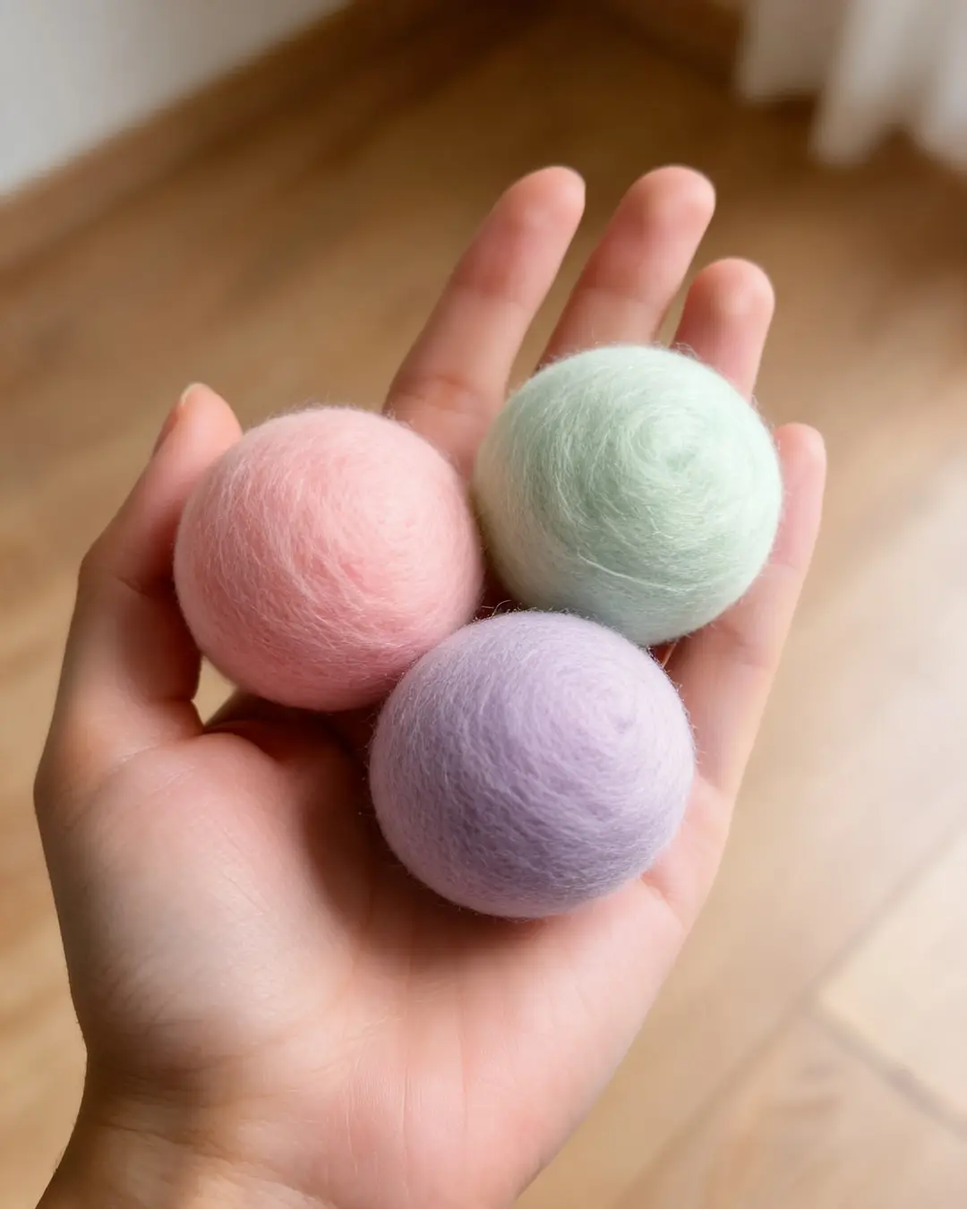 Una mano con tres pelotas de fieltro pastel
